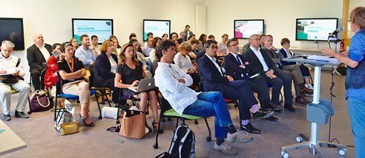 Assemblée de personnes assises écoutant une conférencière dans une salle numérique