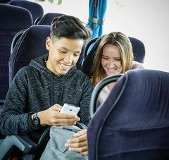 2 lycéens assis dans le car regardent un téléphone et sourient 